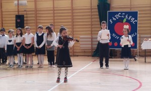 Uczniowie klas drugich, którzy śpiewają, recytują wiersze i grają na skrzypcach.